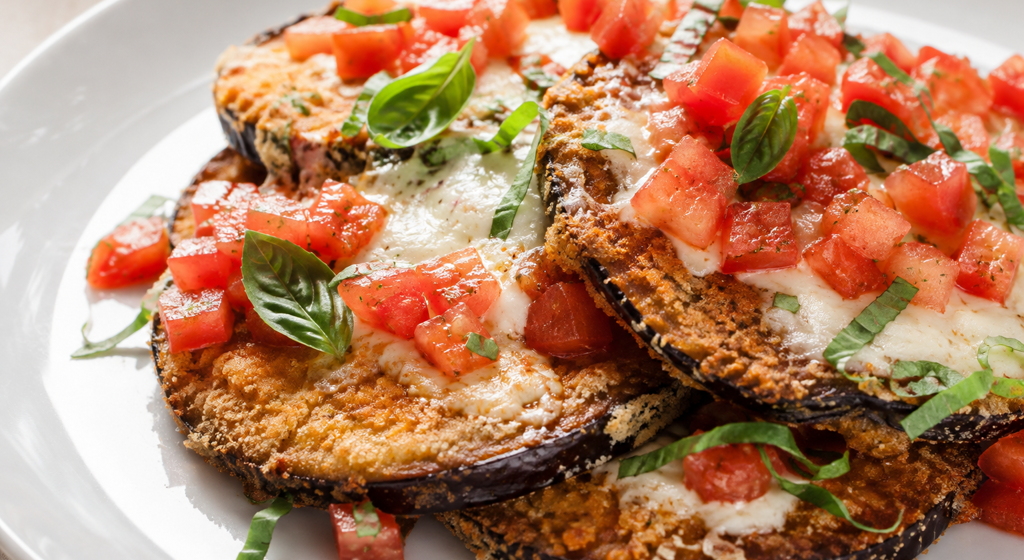 Panierte Auberginenscheiben mit geschmolzenem Mozzarella, frischen Tomaten und Basilikum.